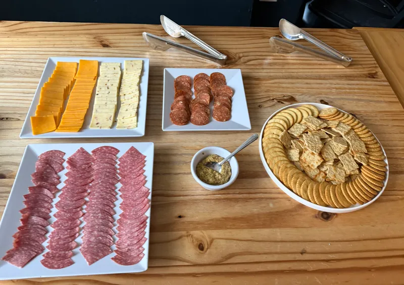 A Monday Tasting salad bar spread: sliced cheddar and herbed cheese, salami and pepperoni, crackers, and grainy mustard