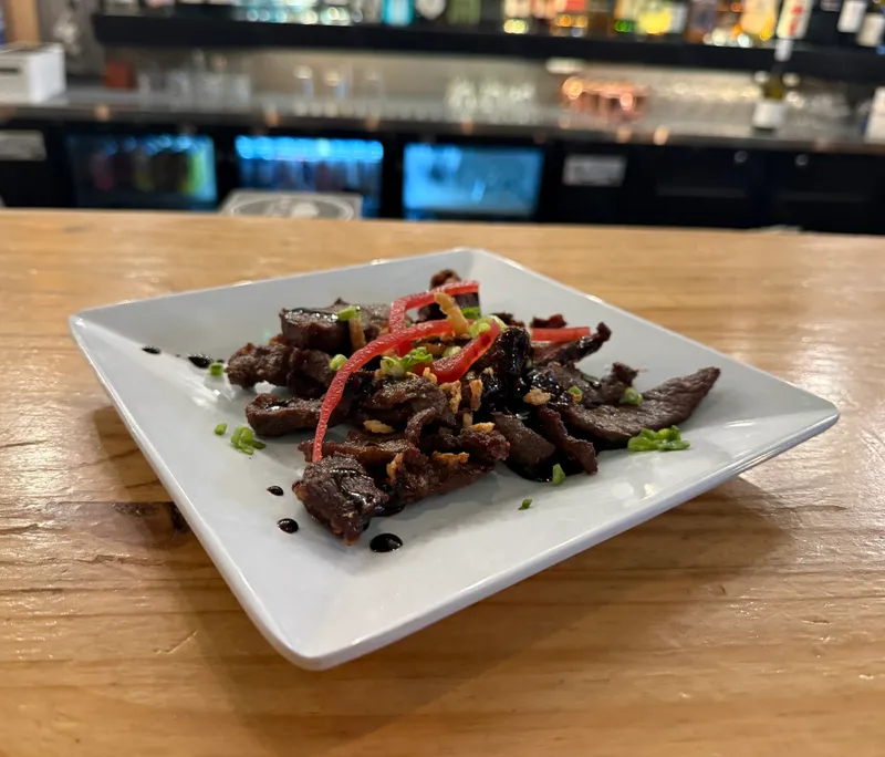 Charred steak bites with a sweet glaze, pickled and crispy onion, plated at the bar