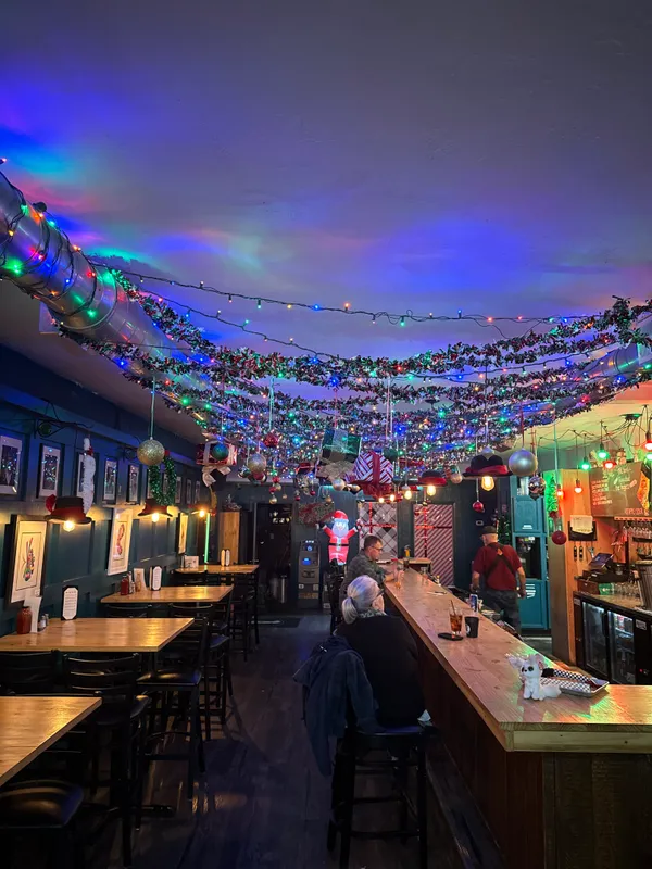 The bar draped in a canopy of colorful Christmas lights and garland with a festive ceiling light show