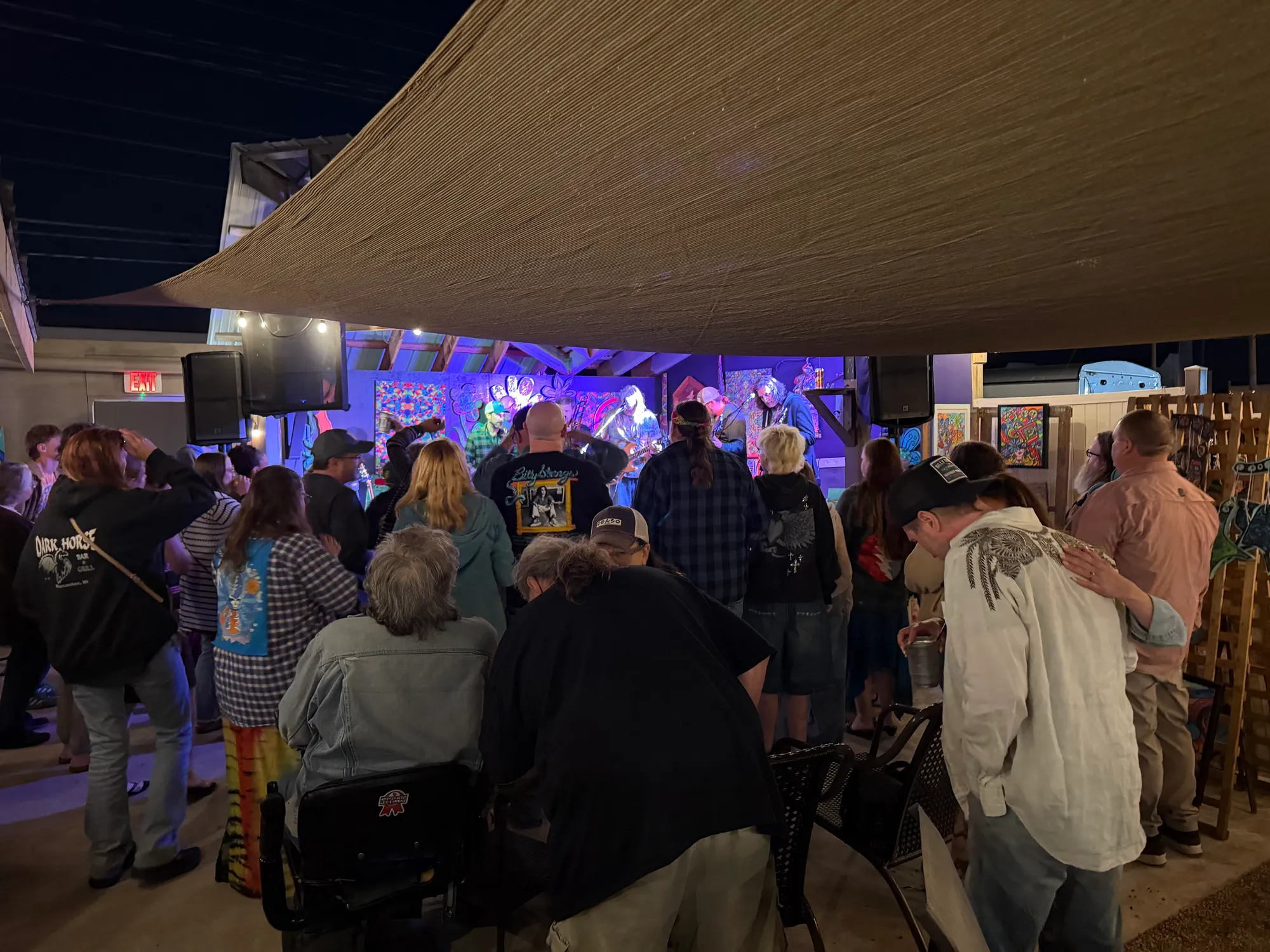 A crowd gathered for live music on a colorful stage at an outdoor evening event on the patio